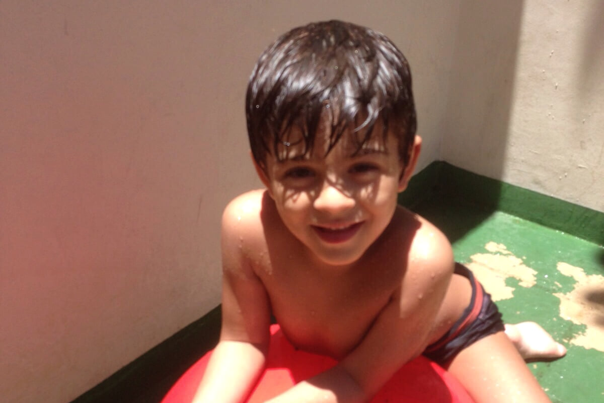 Gustavo pequeno sorrindo e apoiando as mãos em uma bola vermelha